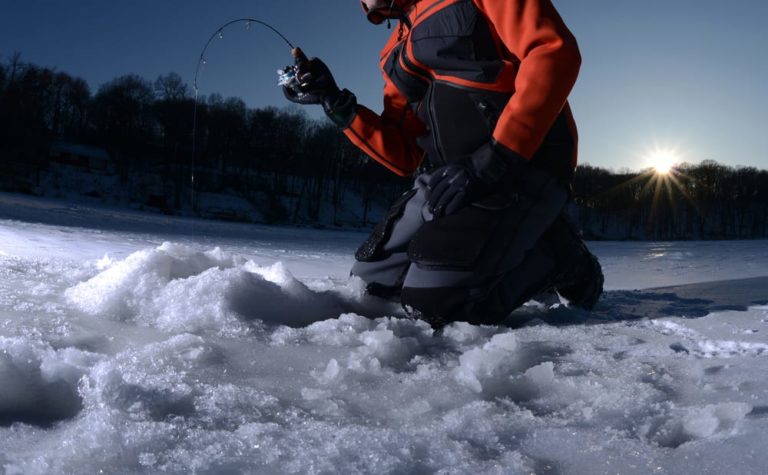 a man knelt by an ice fishing hole