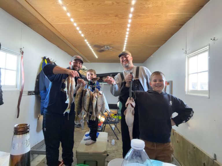 Family Multi Fish Stringer Ice House A group of people in an ice house holding a stringer of several fish caught ice fishing.