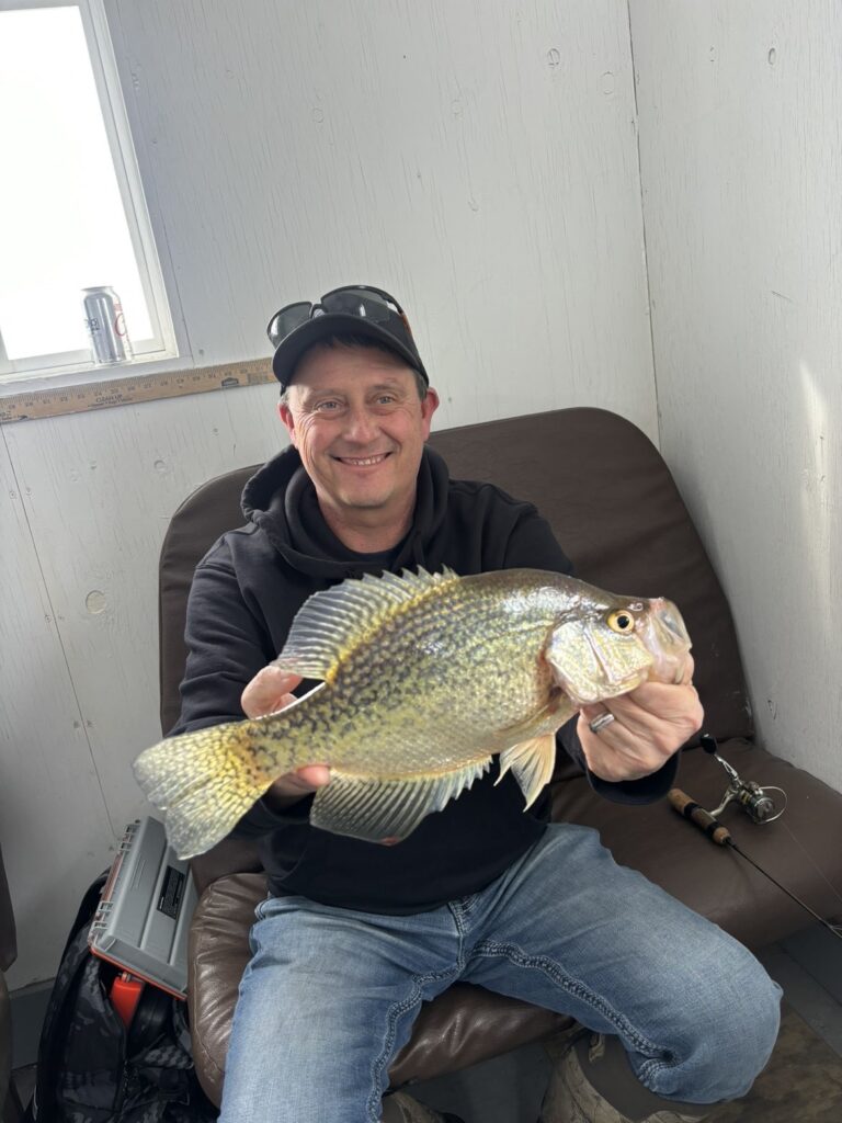 Giant Slab Crappie Ice Fishing Man seated in an ice house holding a large crappie.