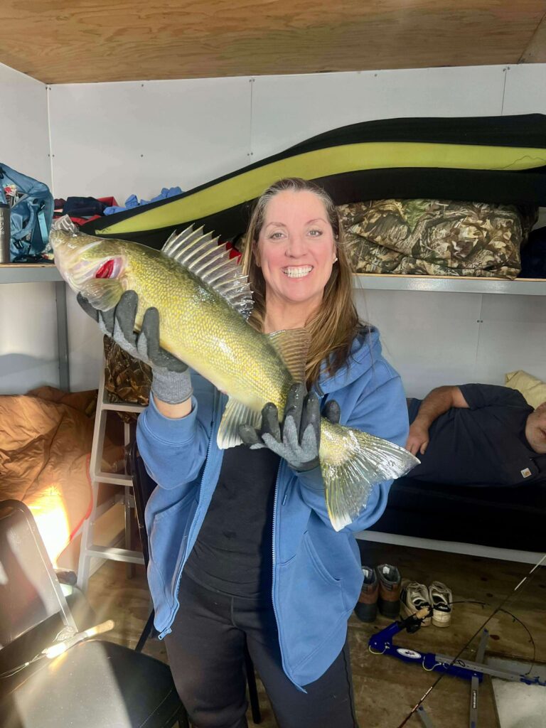 Trophy Walleye Ice Fishing Success Woman in a blue jacket holding a large walleye inside an ice house.